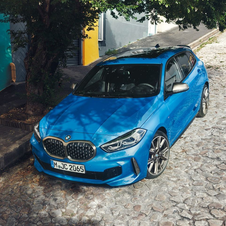 BMW 1-sarjan auto kadunvarteen pysäköitynä. BMW 1-sarjan auto, Misano Blue metalliväri, 3/4-näkymä etuosasta lintuperspektiivistä.