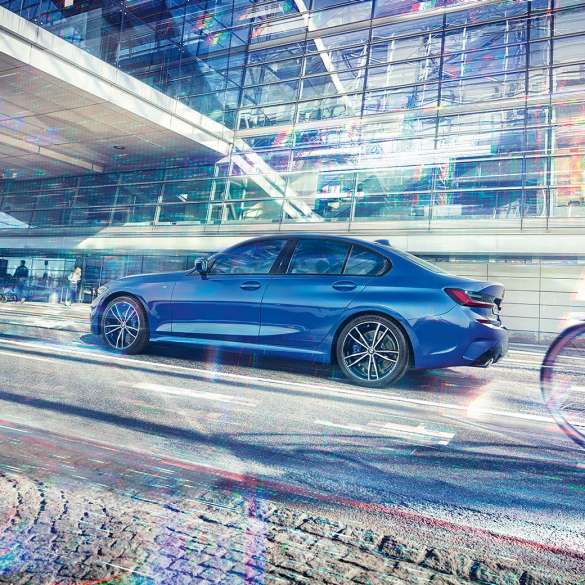 BMW 3-sarjan Sedan sivultapäin. Sivukuva paikallaan olevasta BMW 3-sarjan Sedanista päivänvalossa lasisen rakennuksen edessä.
