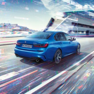 BMW 3-sarjan Sedan, sivukuva perästä. Kolmeneljäsosakuva BMW 3-sarjan Sedanin perästä päivänvalossa suurkaupunkiympäristössä.