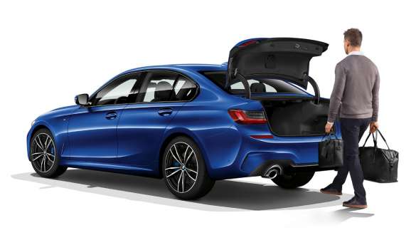 BMW 3-sarjan Sedan (G20), takaluukun automatiikka. Kolmen neljäsosan näkymä pysähtyneenä olevan BMW 3-sarjan Sedanin (G20) perästä ja kuljettajasta, joka avaa jalalla takaluukun.