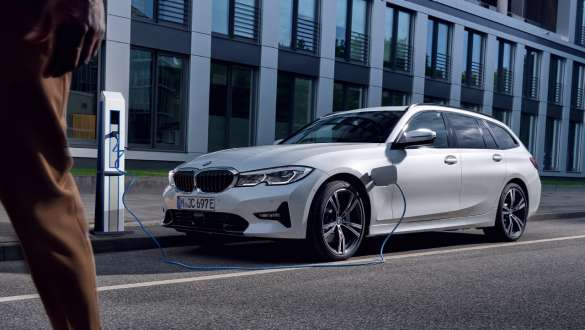 Plug-in Hybrid, BMW 3-sarjan Touring 2021 G21, kolmen neljäsosan näkymä latauksessa olevan auton keulasta Plug-in Hybrid, BMW 3-sarjan Touring 2021 G21, kolmen neljäsosan näkymä rakennuksen edessä latauksessa olevan auton keulasta