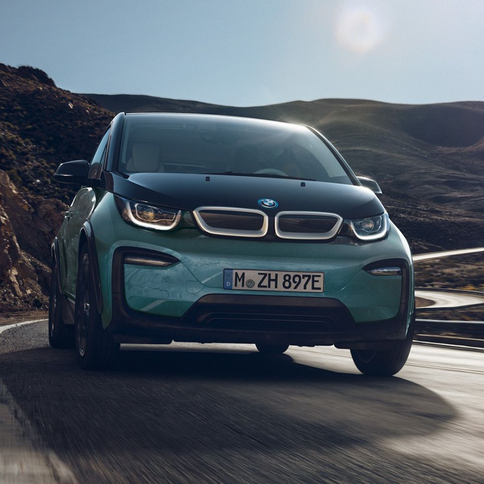 BMW i3 2018 sivunäkymä ajaen BMW i3 I01 2018 Jucaro Beige, korostuksella Frozen Grey -metalliväri, sivunäkymä ajaen kaupunkiympäristössä