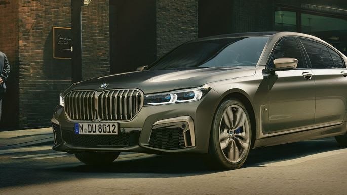 BMW M760Li xDrive Sedan kaupunkimaisemassa BMW M760Li xDrive Sedan, sivunäkymä kadulla kaupunkimaisemassa ajavan auton etuosasta