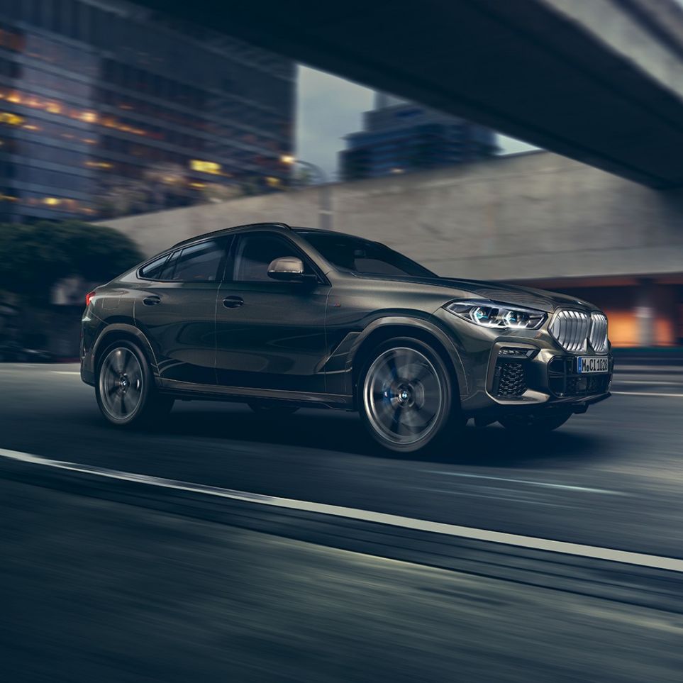 BMW X6 liikkeellä. BMW X6, 3/4-näkymä edestä auton ajaessa kaupunkinäkymän edessä.