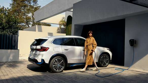 Kvinna som laddar sin BMW iX1 på uppfarten hemma. Kvinna som laddar sin BMW iX1 på uppfarten hemma.