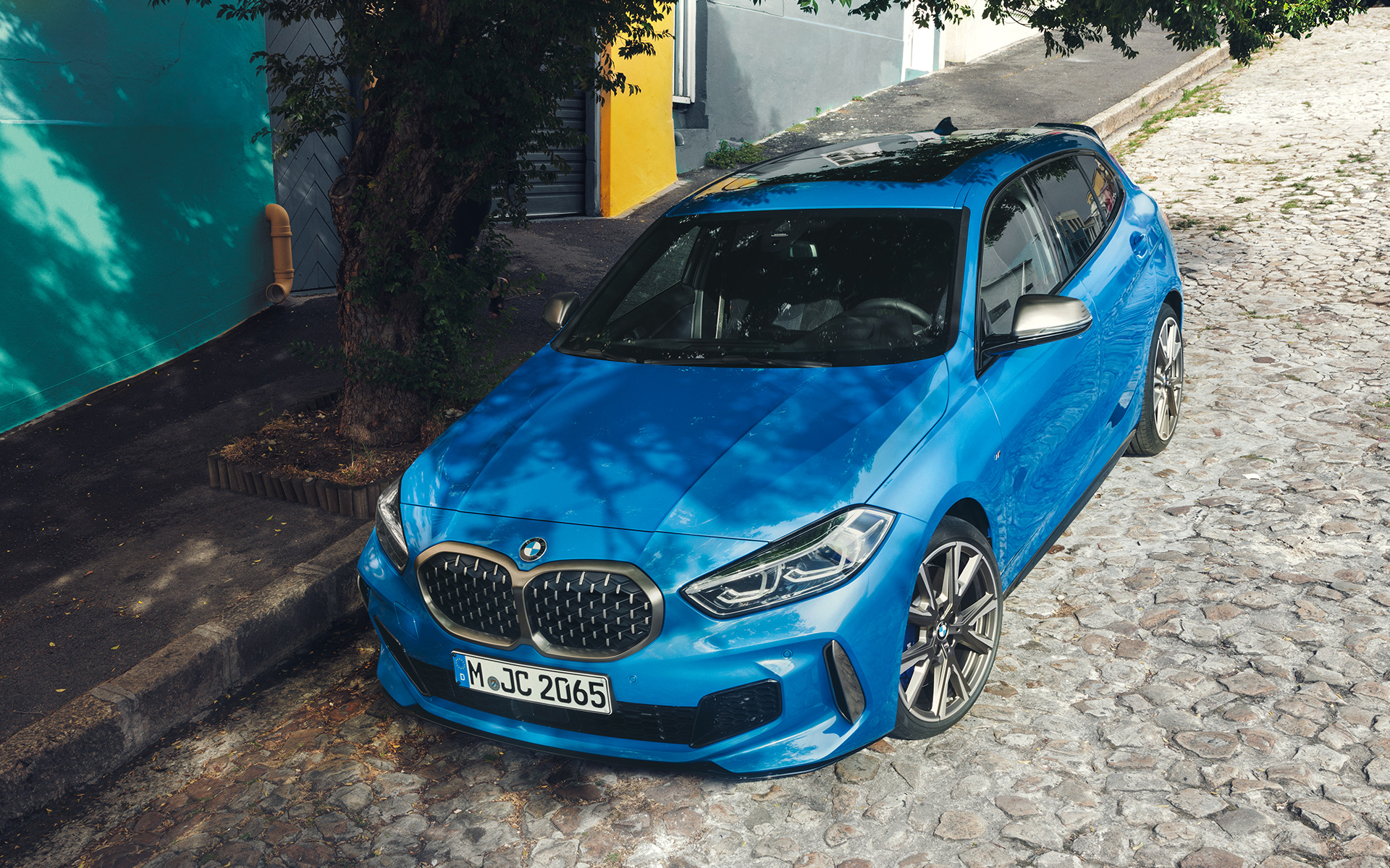 BMW 1-sarjan M135i F40, Misano Blue metalliväri, 3/4-näkymä etuosasta kadun varrelle pysäköitynä lintuperspektiivistä.