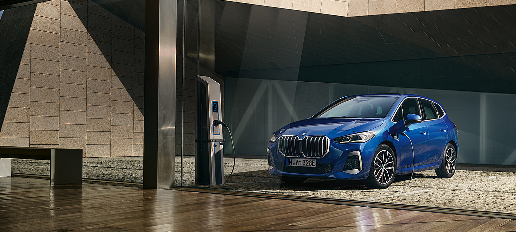 BMW 2-sarjan Active Tourer 230e Plug-in Hybrid U06 2021 metalliväri M Portimao Blue, kolmen neljäsosan näkymä lataustolpan luona olevan auton keulasta