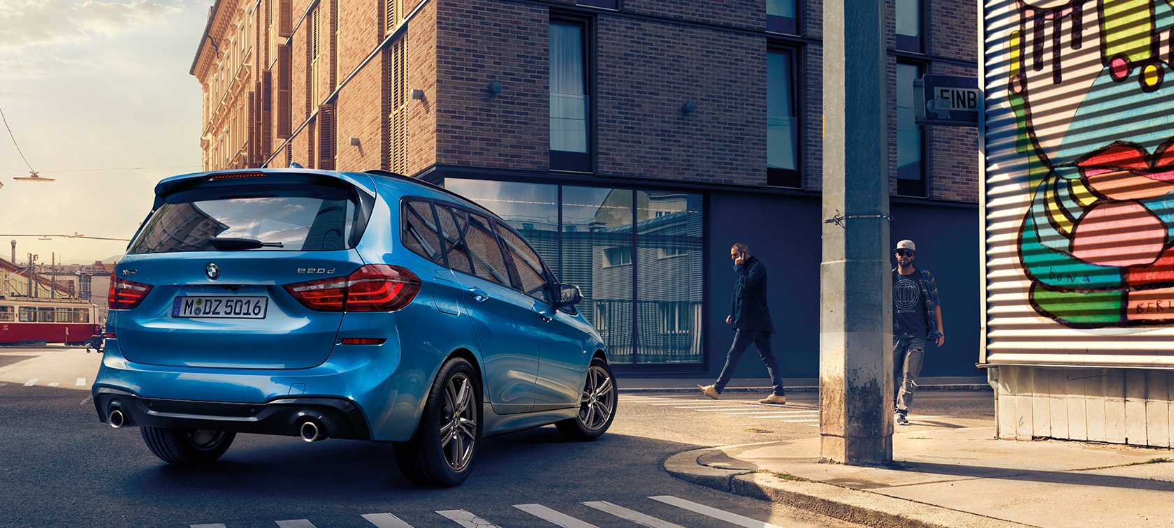 BMW 2-SARJAN Gran Tourer lintuperspektiivistä Mies seisoo Estoril Blue -metallivärisen BMW 2-SARJAN Gran Tourer F46 Facelift 2018 -auton vieressä, kadulla pysäköitynä oleva auto lintuperspektiivistä