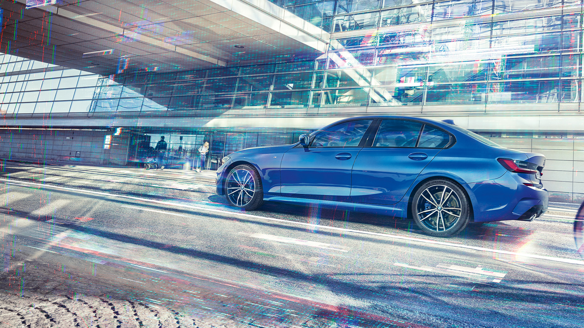 BMW 3-sarjan Sedan sivultapäin. Sivukuva paikallaan olevasta BMW 3-sarjan Sedanista päivänvalossa lasisen rakennuksen edessä.