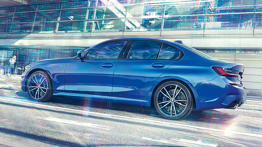 BMW 3-sarjan Sedan (G20) päivällä lasirakennuksen edessä Sivukuva paikallaan olevasta, Portimao Blue -värisestä BMW 3-sarjan Sedanista (G20) päivällä lasirakennuksen edessä