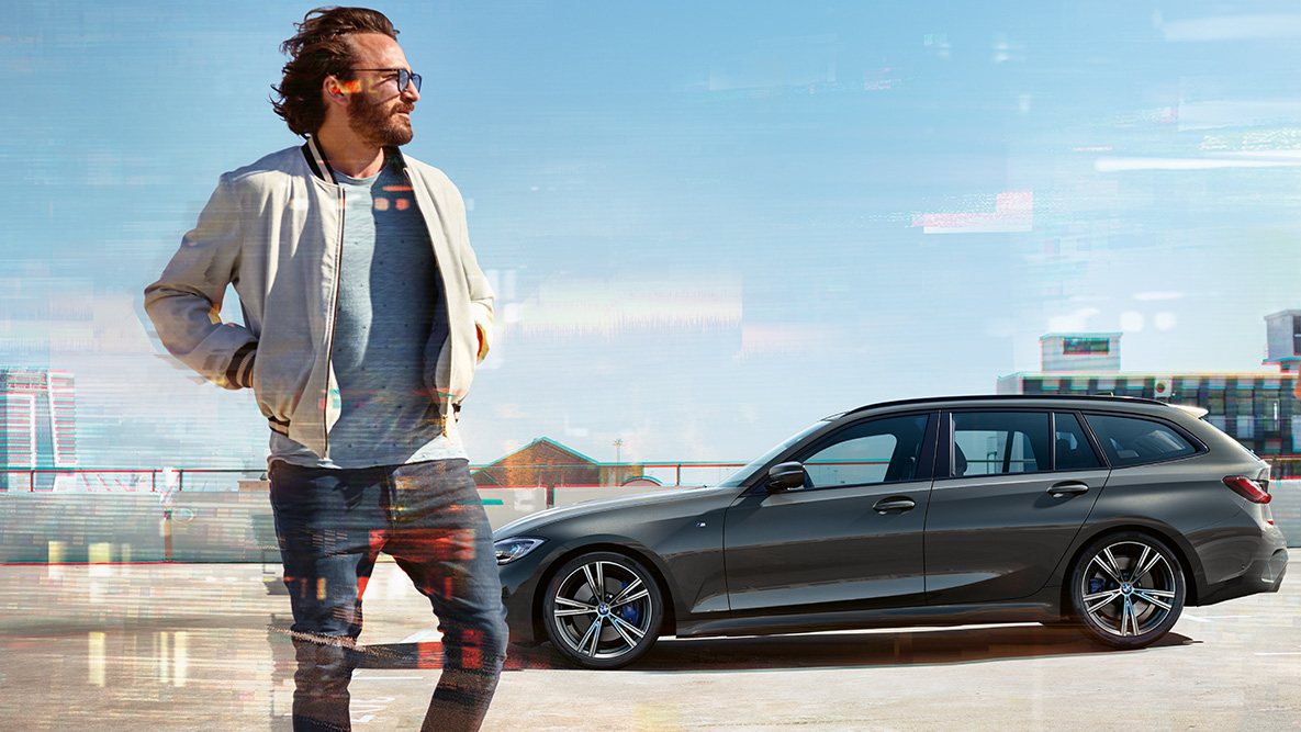 BMW 3-sarjan Touring (G21), kolmen neljäsosan näkymä keulasta, muotoilu BMW 3-sarjan Touring (G21) Dravite Grey, kolmen neljäsosan näkymä keulasta auton ajaessa sillalla maaseudulla