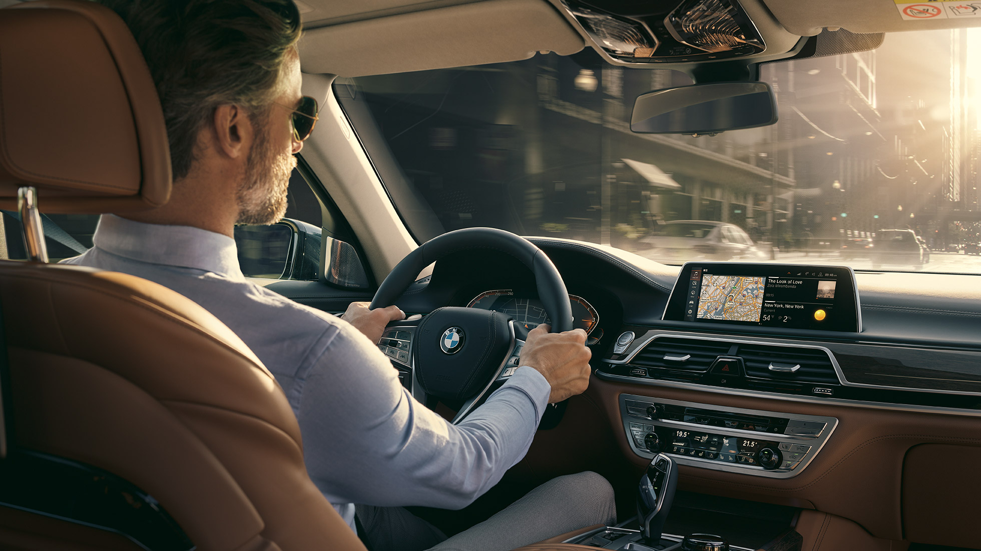 BMW 7-sarjan Sedanin Connectivity-ominaisuudet BMW 7-sarjan Sedan: Mies istuu BMW:ssä ja käyttää Connectivity-ominaisuuksia