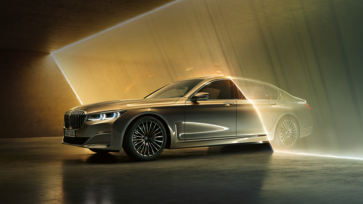 BMW 7-sarjan Sedan, josta näkyy kolme neljäsosaa edestä BMW 7-sarjan Sedan: Harmaa BMW, josta näkyy kolme neljäsosaa edestä valon ympäröimänä