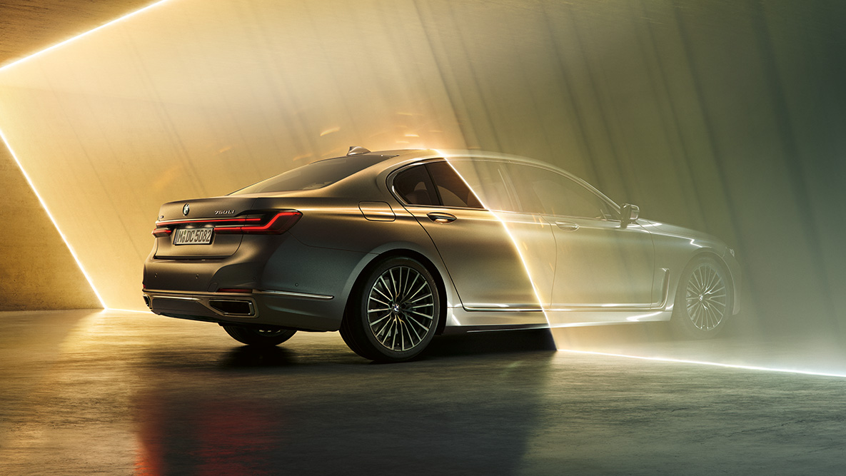 Bernina Grey -värinen BMW 7-sarjan Sedan Kolme neljäsosanäkymä Bernina Grey -värisen BMW 7-sarjan Sedanin takaosasta valon ympäröimänä
