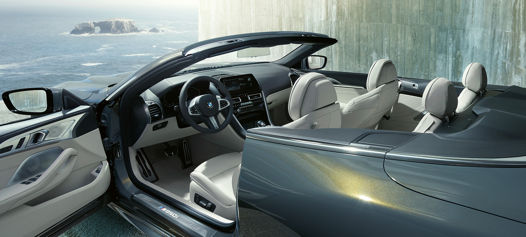 Dravit Grey -metallivärinen BMW M850i xDrive, sivulta kuvattuna, kangaskatto ja ovi auki. Dravit Grey -metallivärinen BMW M850i xDrive, sivulta kuvattuna, kangaskatto ja ovi auki.