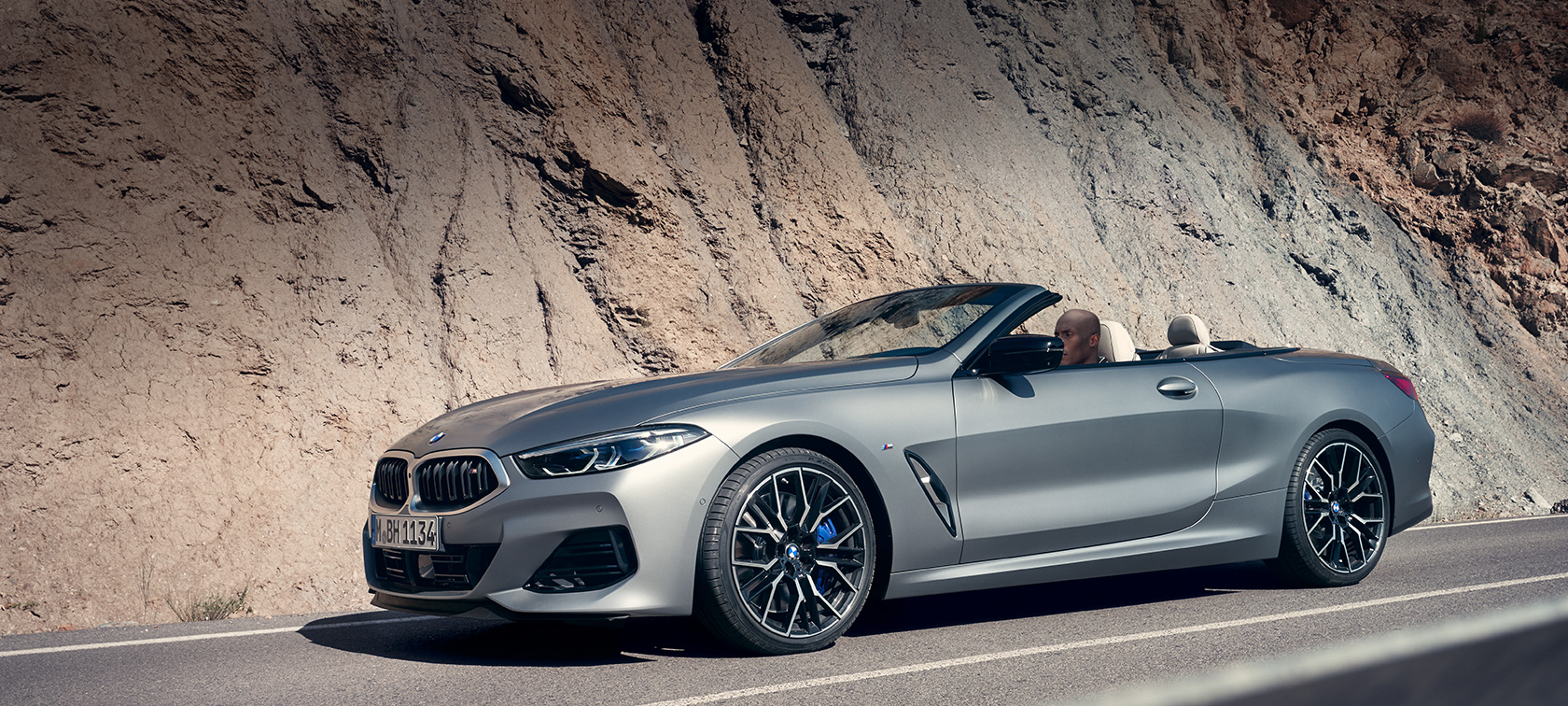 BMW 8-sarjan konvertoitava G14 LCI Facelift 2022 katon ollessa avoinna auton ajaessa vuorenseinämää pitkin BMW 8-sarjan konvertoitava G14 LCI Facelift 2022 BMW Individual Frozen Pure Grey -metalliväri, näkymä katon ollessa avoinna auton ajaessa vuorenseinämää pitkin