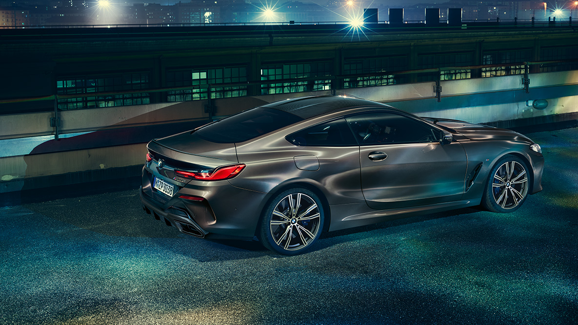 Sivukuva paikallaan olevasta BMW 8-sarjan Coupésta. Paikallaan oleva BMW 8-sarjan Coupé, jossa on BMW Individual -varustelu, kuvattuna sivulta yöllä kaupunkinäkymän edessä.