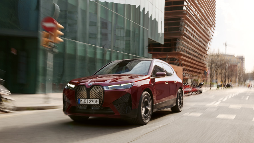 BMW iX i20, sähköinen SUV, BMW iX xDrive50, kuljettajan avustinjärjestelmät BMW iX i20 2021, sähköinen SUV, BMW iX xDrive50 Aventurine Red liikkeellä urbaanissa ympäristössä
