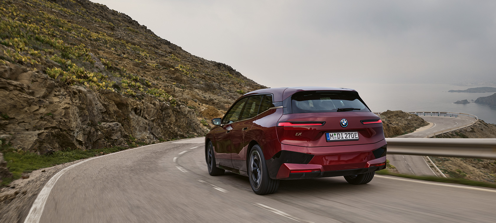 BMW iX i20 2021, sähköinen SUV, BMW iX xDrive50 liikkeellä rantatiellä BMW iX i20 2021, sähköinen SUV, BMW iX xDrive50, Aventurine Red, näkymä rantatiellä ajavan auton perästä