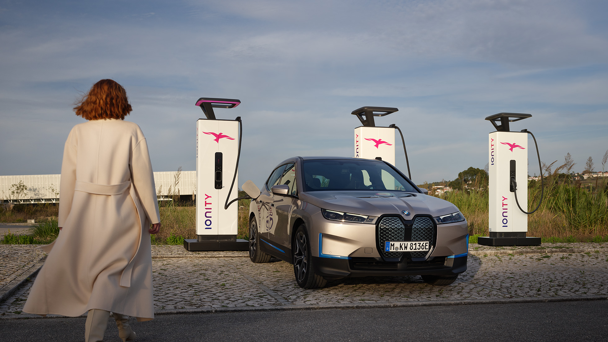 BMW iX, kolmen neljäsosan näkymä keulasta latausaseman luona BMW iX Cashmere Silver i20, kolmen neljäsosan näkymä keulasta latausaseman luona