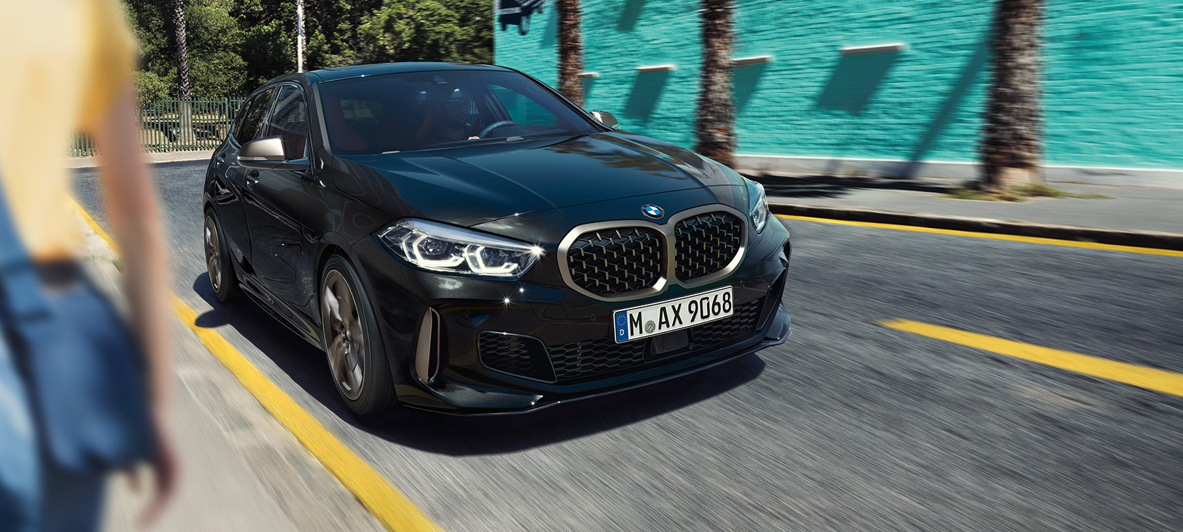 BMW M135i xDrive, 3/4 näkymä keulasta. BMW M135i xDrive, metalliväri Sapphire Black, 3/4 sivunäkymä ajavasta autosta.