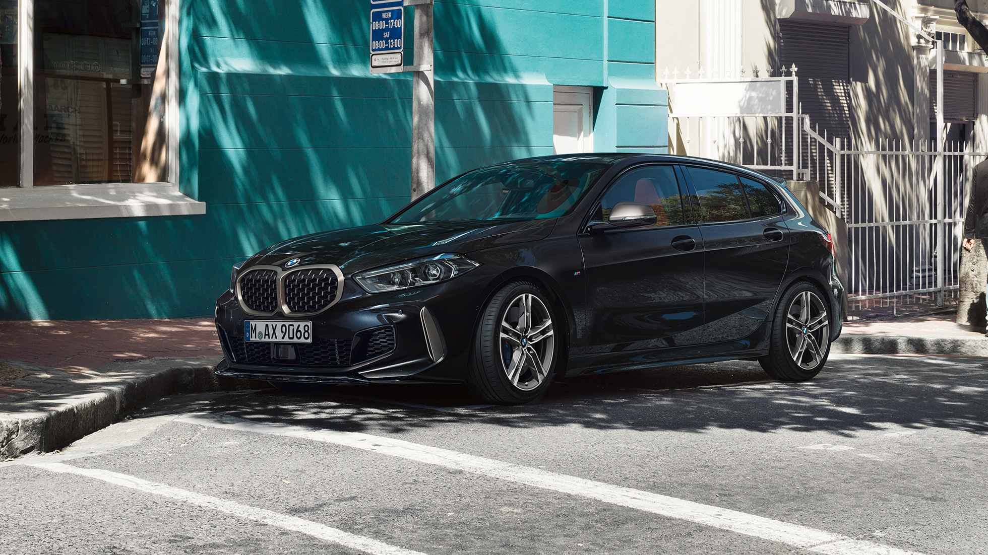 BMW M135i xDrive, 3/4 sivunäkymä. BMW M135i xDrive, metalliväri Sapphire Black, 3/4 sivunäkymä pysäköitynä.