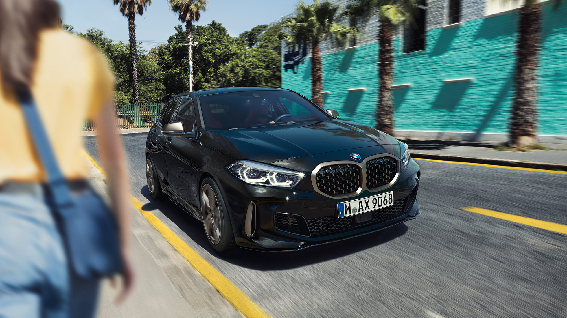 BMW M135i xDrive, 3/4 näkymä keulasta. BMW M135i xDrive, metalliväri Sapphire Black, 3/4 etunäkymä ajavasta autosta nainen etualalla.