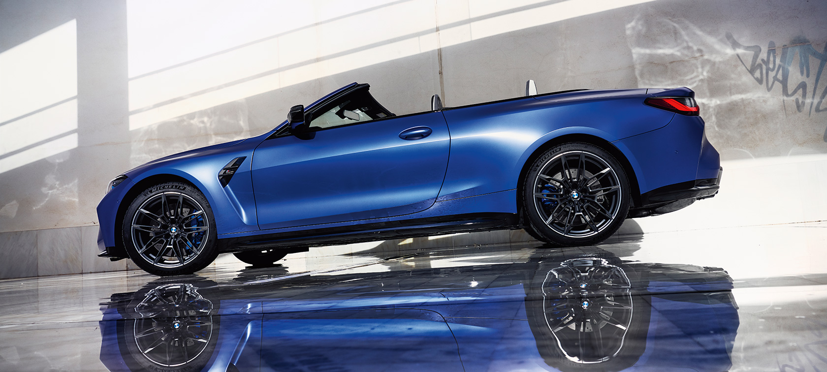 BMW M4 Competition Cabrio jossa M xDrive G83 2021 kolmen neljäsosan sivunäkymä ajavasta autosta BMW M4 Competition Cabrio, jossa M xDrive G83 2021 BMW Individual Frozen Portimao Blue metalliväri 3/4-näkymä edestä ajamassa