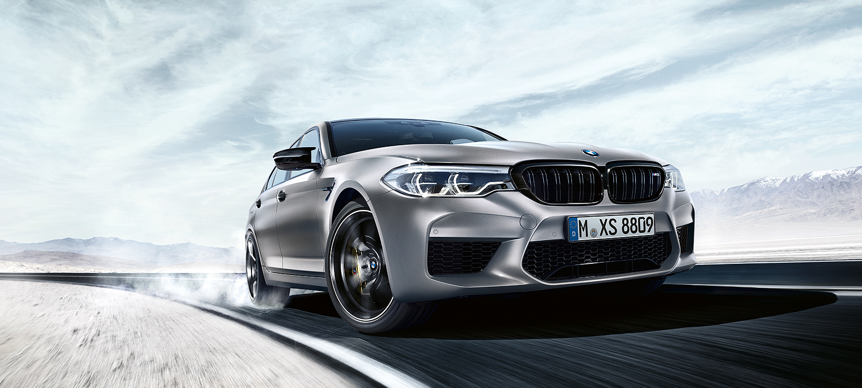BMW M5 Competition toiminnassa Harmaa BMW M5 Competition ajaa moottoritiellä taustallaan aavikkomaisema