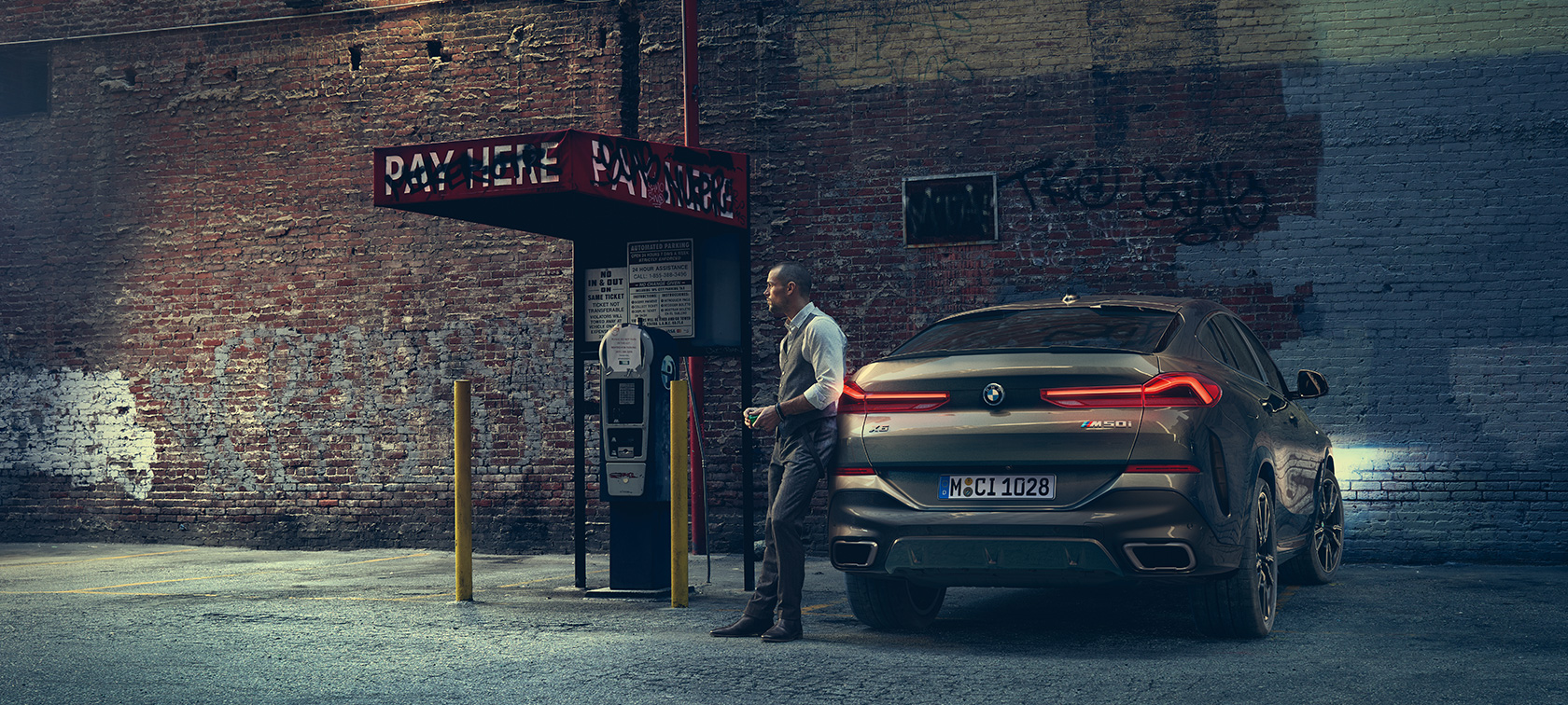 BMW X6 M50i.:n perä. Mies nojaa BMW X6 M50i:n perään.