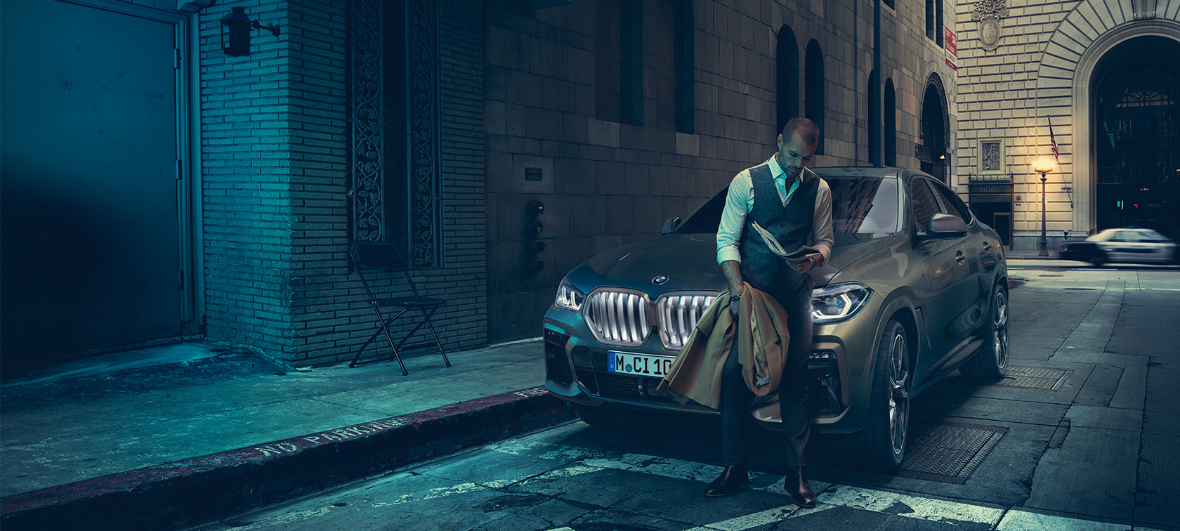 BMW X6 M50i:n keula. Mies nojaa BMW X6 M50i:n keulaan.