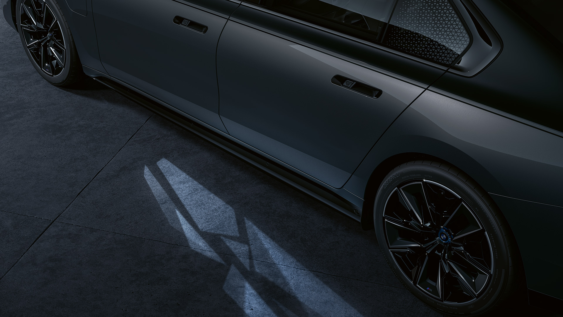 Valokonsepti BMW M760e xDrive Sedan G70 Valokonsepti BMW M760e xDrive Sedan G70 Two-Tone -ulkoväri Black Sapphire metallic BMW Individual -metalliväri Dravite Grey lähikuva sivulta päällekytketyllä Welcome Light Carpet