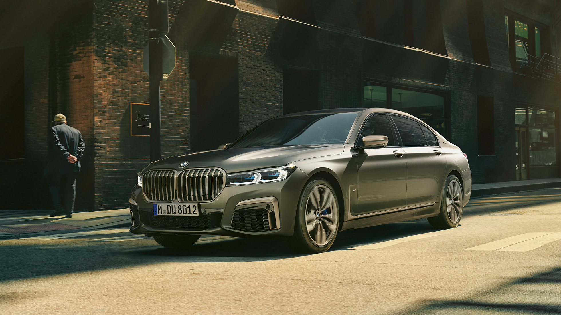 BMW M760Li xDrive Sedan kaupunkimaisemassa BMW M760Li xDrive Sedan, sivunäkymä kadulla kaupunkimaisemassa ajavan auton etuosasta
