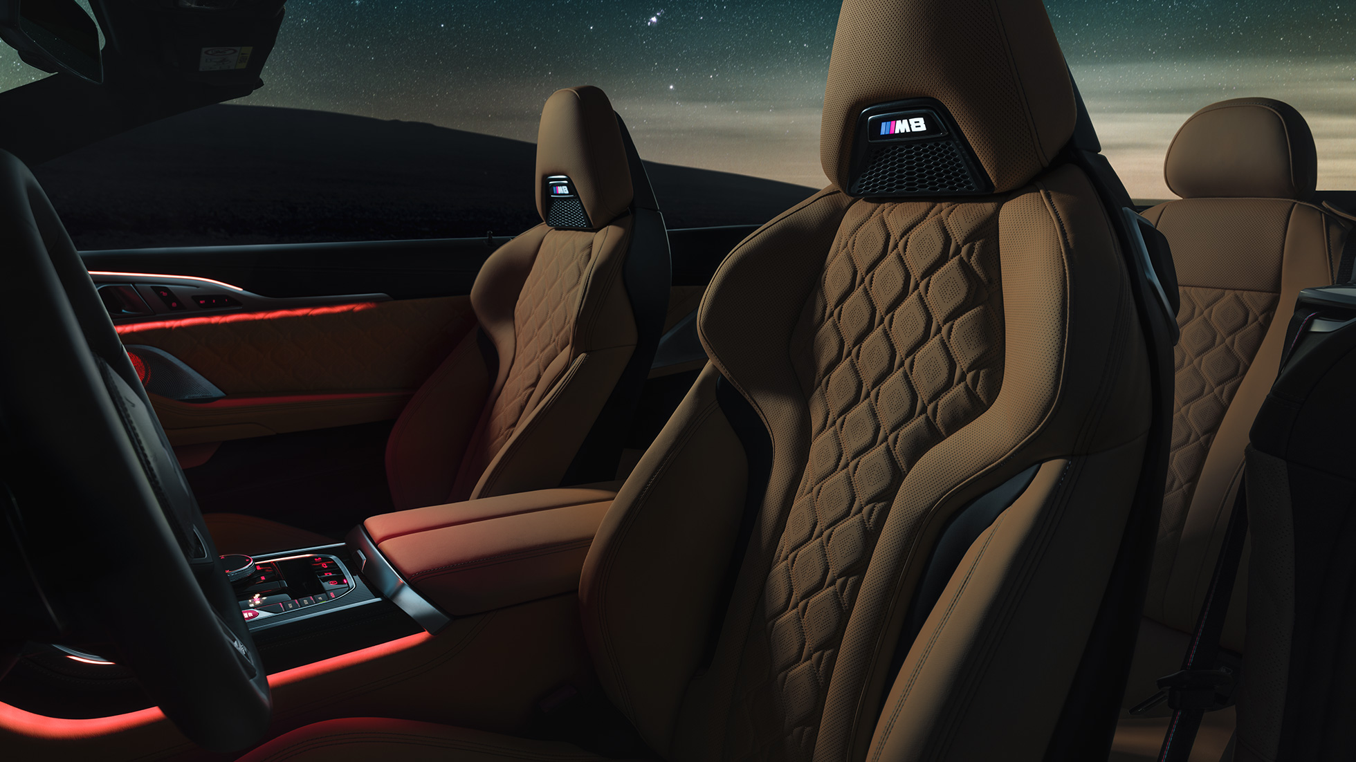 Merino-nahkaiset M urheiluistuimet. BMW M8 Competition Cabrio katto avattuna tähtitaivaan alla, sisätilassa Merino-nahkaiset M urheiluistuimet ja punainen tunnelmavalaistus.