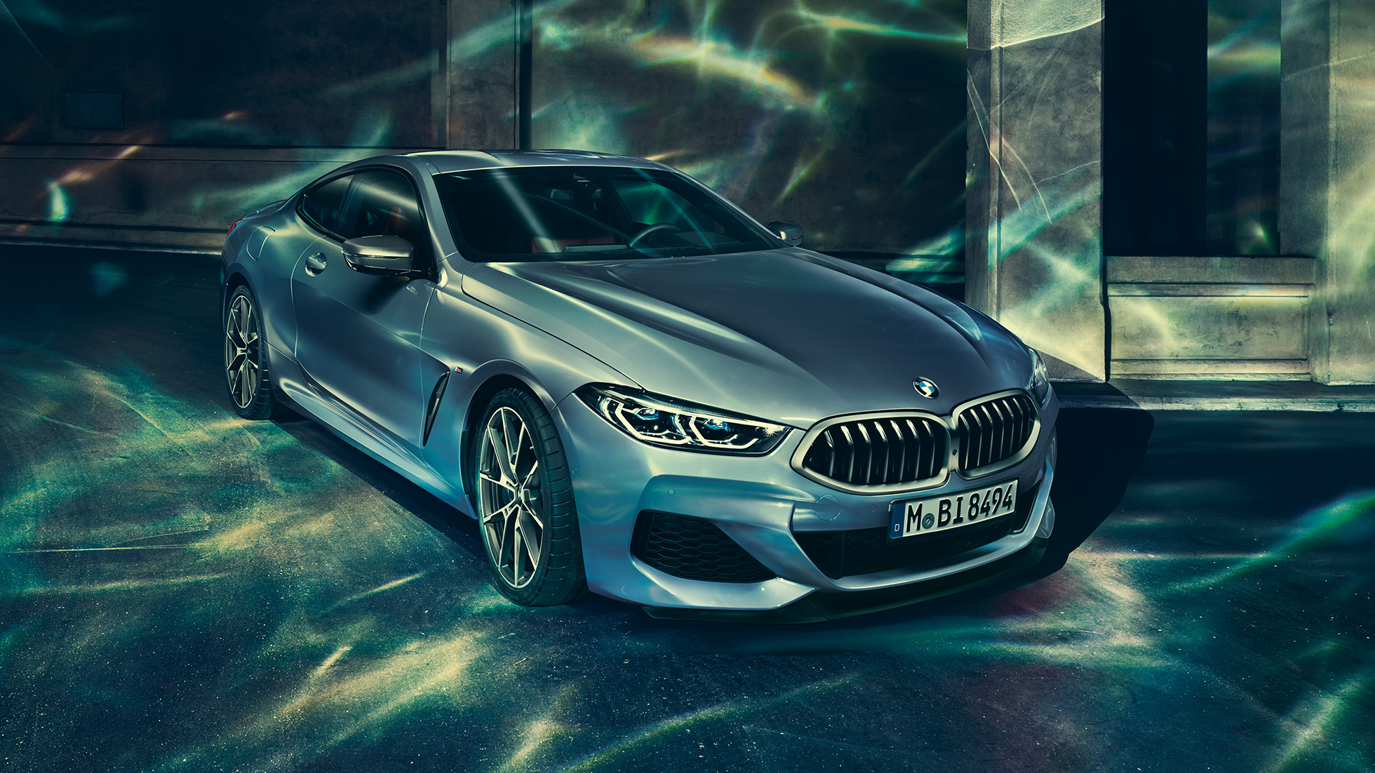 BMW M850i xDrive Coupé, 3/4-näkymä edestä vasemmalta. BMW M850i xDrive Coupé metallivärissä Barcelona Blue, 3/4-näkymä edestä vasemmalta auton ollessa pysähtyneenä rakennuksen edessä.