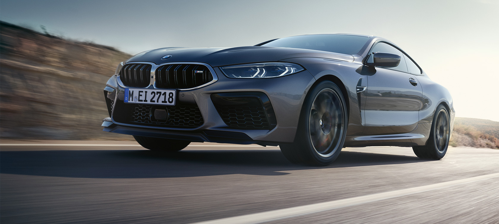BMW M8 Coupé F92 LCI Facelift 2022 3/4-näkymä auton ajaessa BMW M8 Coupé F92 LCI Facelift 2022 Skyscraper Grau -metalliväri 3/4-näkymä sivulta auton ajaessa, sammakkoperspektiivi