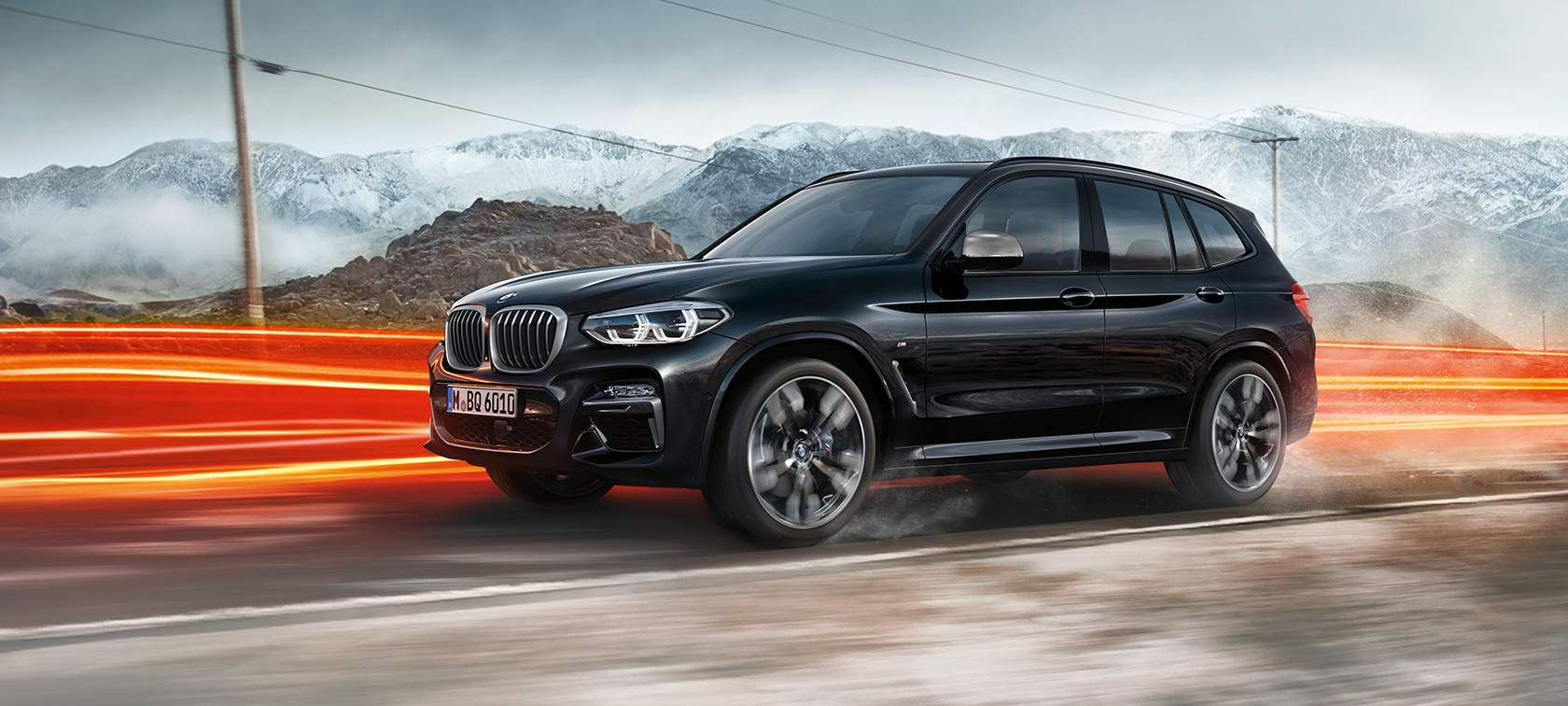 BMW X3 M40i ja BMW X3 M40d, sivunäkymä. BMW X3 M40i ja BMW X3 M40d, metalliväri Sapphire Black, ajaa, ulkopuoli, sivunäkymä ja valot vuoristomaiseman edessä.