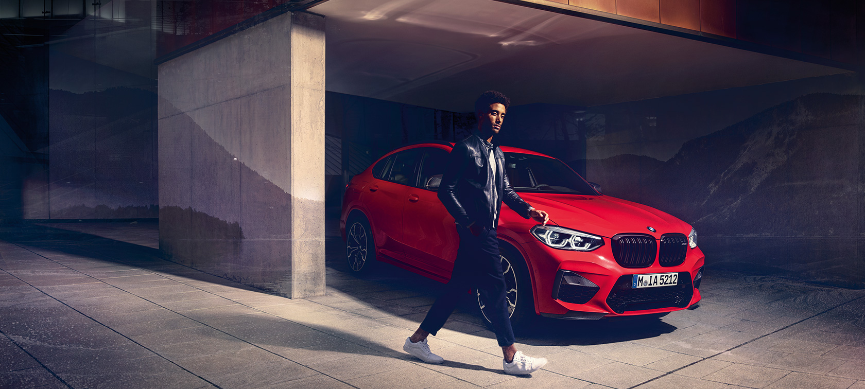 BMW X4 M Competition, metallivärinä Toronto Red, ulkopuoli, kolme neljäsosan sivunäkymä ja nuori mies.