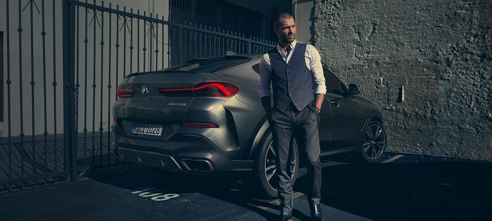 Kolmen neljäsosan näkymä BMW X6 M50i G06:n takaa katsottuna Mies seisoo BMW X6 M50i G06 2018 -auton vieressä, kolmen neljäsosan näkymä SUV:n takaa katsottuna