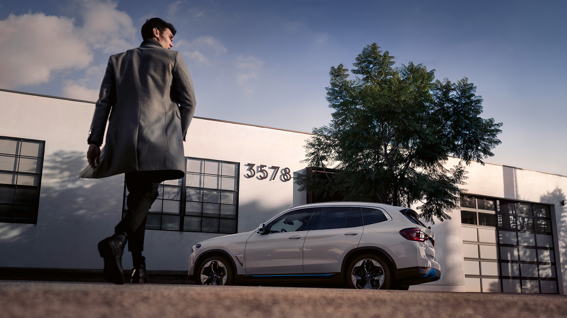 BMW iX3 G08, sivunäkymä rakennuksen edessä ja mies BMW iX3 G08 2020 metalliväri Mineral White, sivunäkymä rakennuksen edessä ja mies