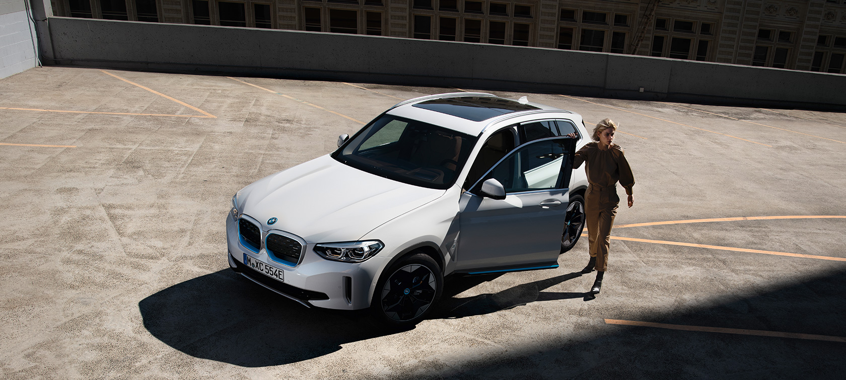 BMW iX3 G08, kolmen neljäsosan näkymä auton keulasta ja nainen BMW iX3 G08 2020 metalliväri Mineral White, kolmen neljäsosan näkymä auton keulasta ja nainen kaupunkiympäristössä