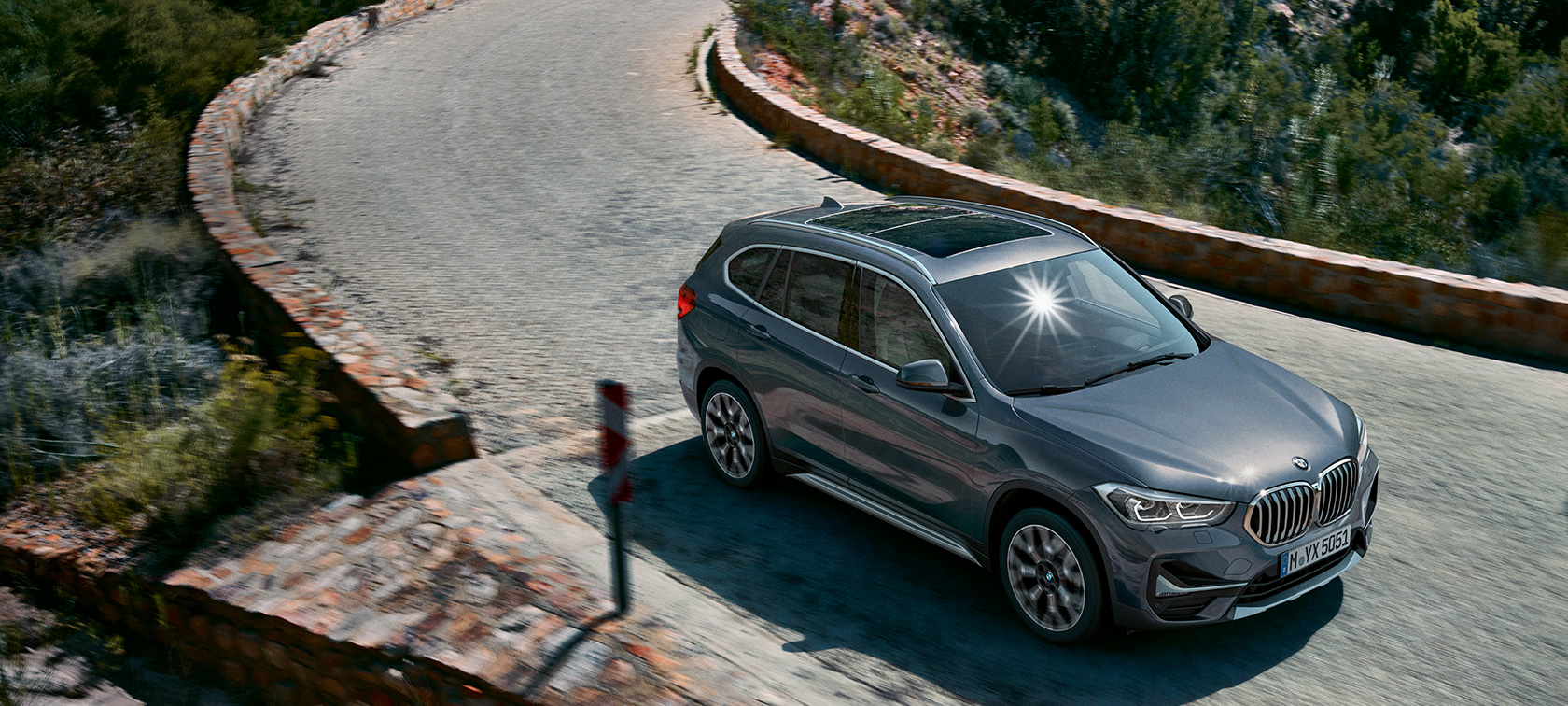 BMW X1, 3/4-näkymä edestä. BMW X1, 3/4-näkymä edestä auton ajaessa vuoristomaiseman edessä.