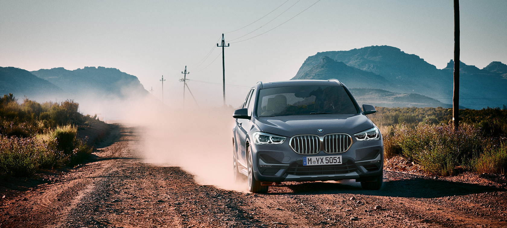 BMW X1, 3/4-näkymä takaa. BMW X1, 3/4-näkymä takaa auton ajaessa vuoristomaiseman edessä.