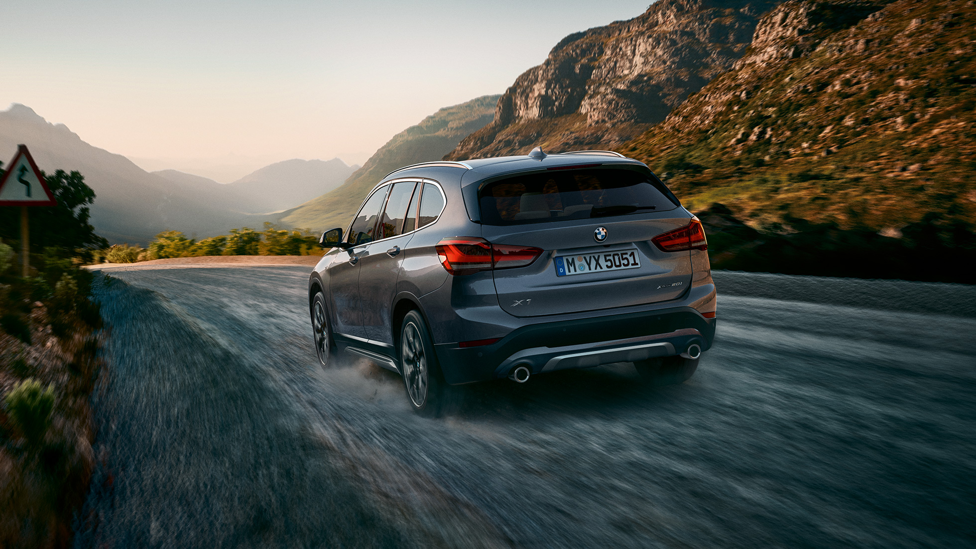 BMW X1, 3/4-näkymä takaa. BMW X1, 3/4-näkymä takaa auton ajaessa vuoristomaiseman edessä.