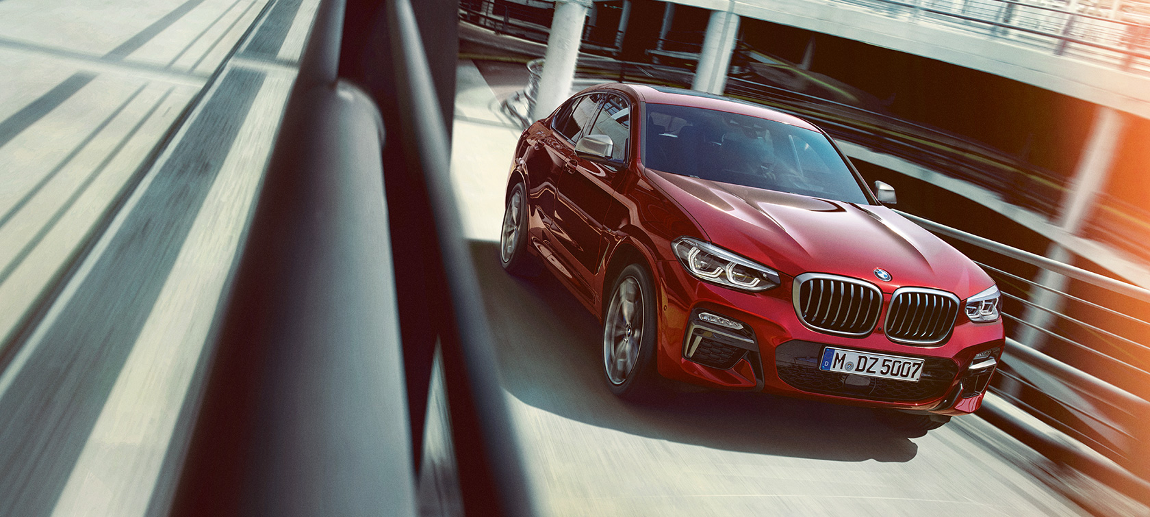 BMW X4 liikkeellä pysäköintitalossa BMW X4 G02 2018 Flamenco Red Brilliant Effect, kolmen neljäsosan sivunäkymä pysäköintitalossa ajavasta autosta