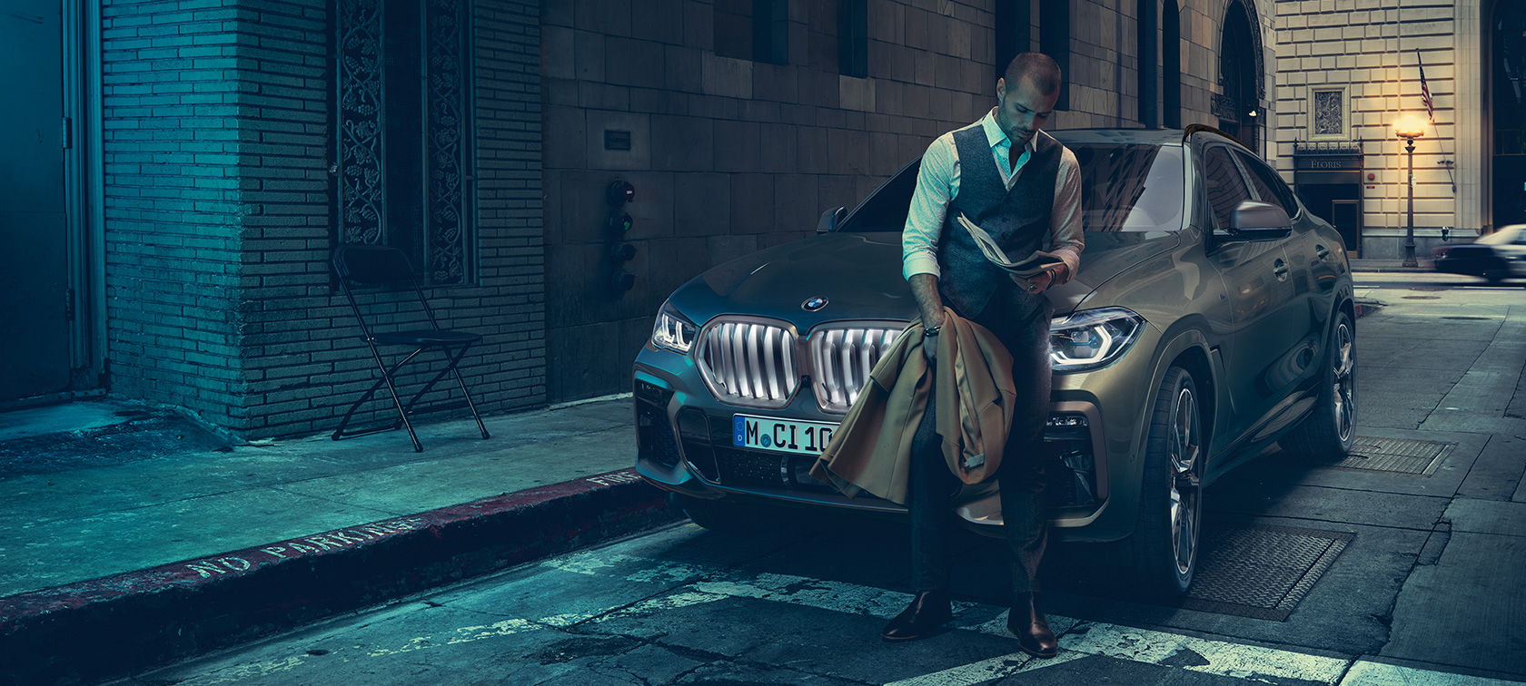 Mies nojaa BMW X6:een. Mies nojaa BMW X6:een, sivunäkymä auton ollessa kaupunkinäkymän edessä.