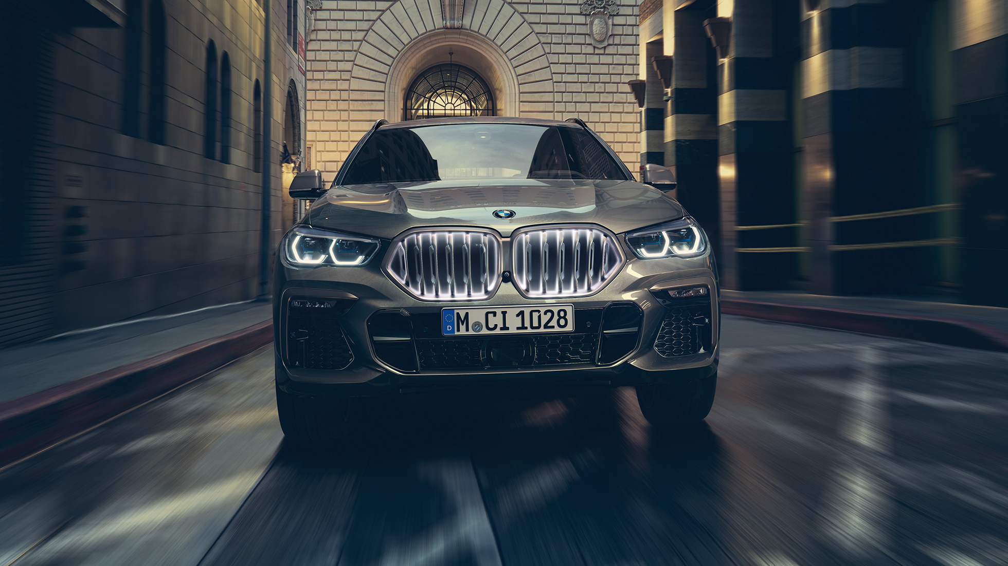 BMW X6, jossa BMW-jäähdyttimensäleikkö Iconic Glow. BMW X6, näkymä edestä kaupunkinäkymän edustalla.