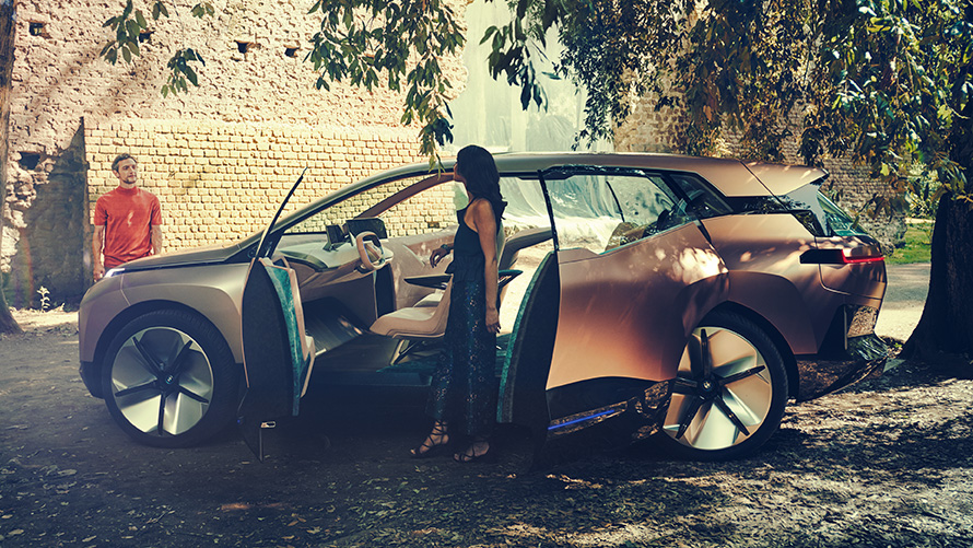 BMW Vision iNEXT sivulta BMW Vision iNEXT sivulta kuvattuna, nainen avoimen oven vieressä ja mies taustalla