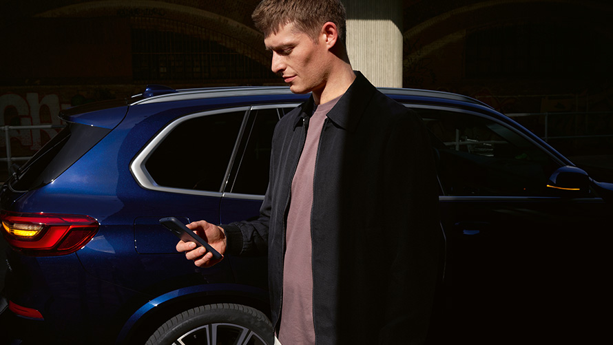 BMW Digital Key – avaimen jakaminen enintään viidelle käyttäjälle BMW Digital Keyn jakaminen enintään viidelle käyttäjälle, mies älypuhelimen kanssa BMW X5 -auton edessä