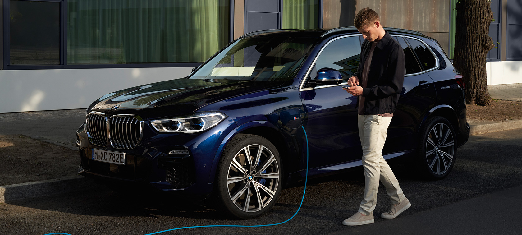 Mies käyttää My BMW -sovellusta älypuhelimella Mies käyttää BMW ConnectedDriven My BMW -sovellusta äypuhelimella BMW X5 Plug-in Hybridin latautuessa